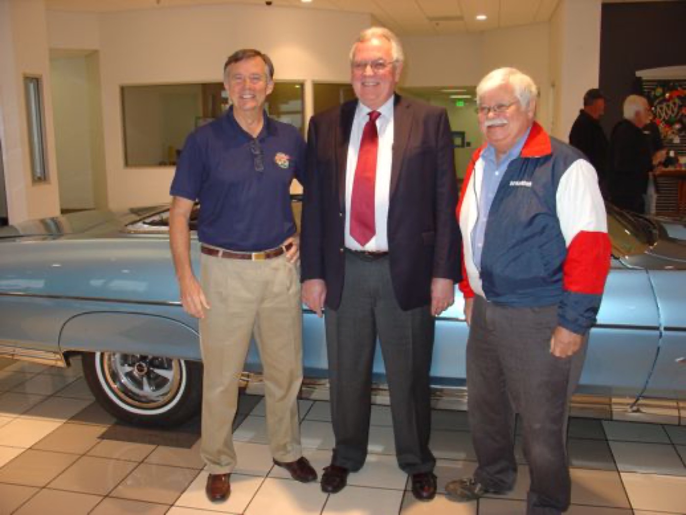 Three club gentlemen smiling by blue convertible