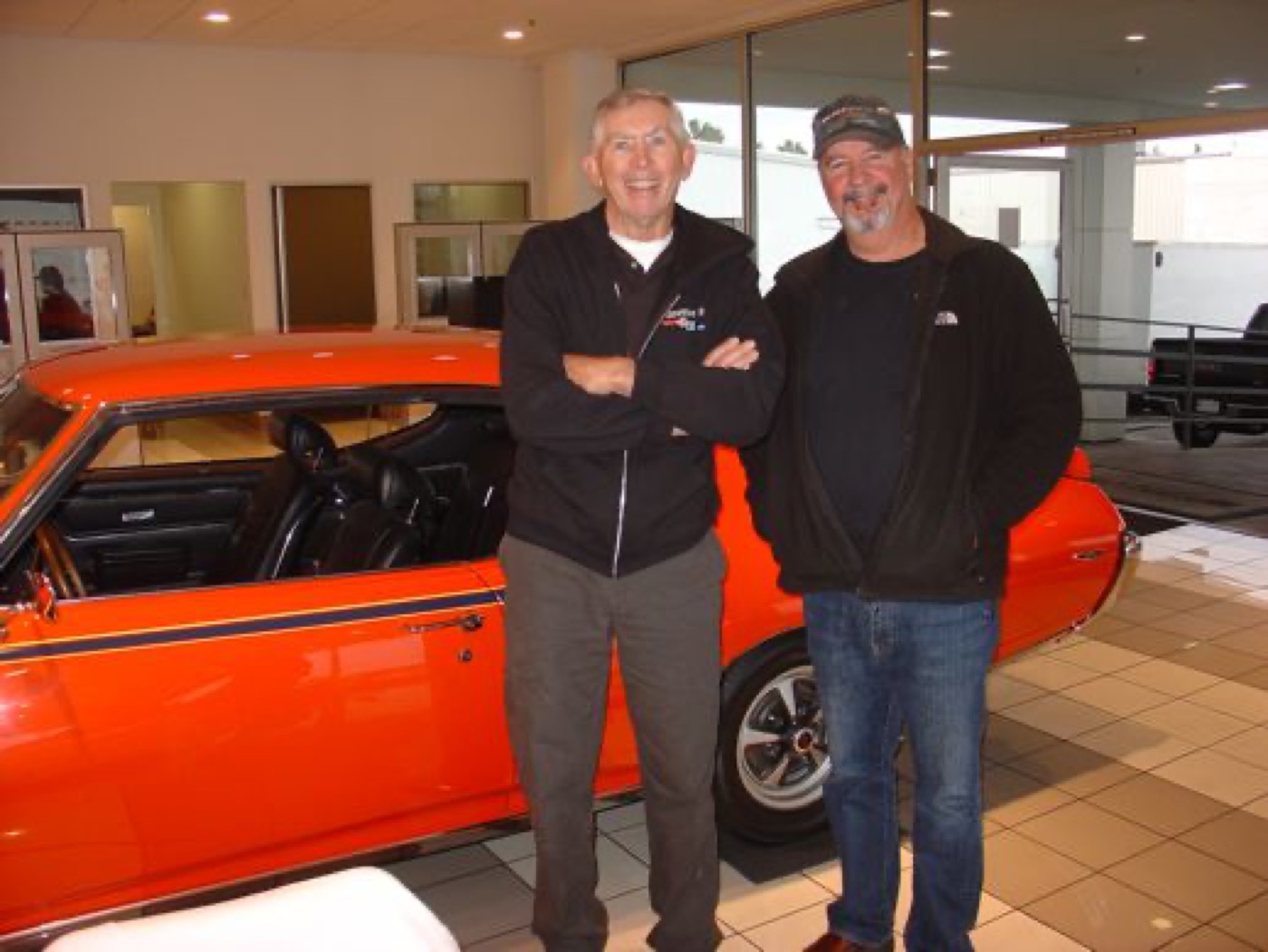 Two friends grinning by orange Pontiac coupe