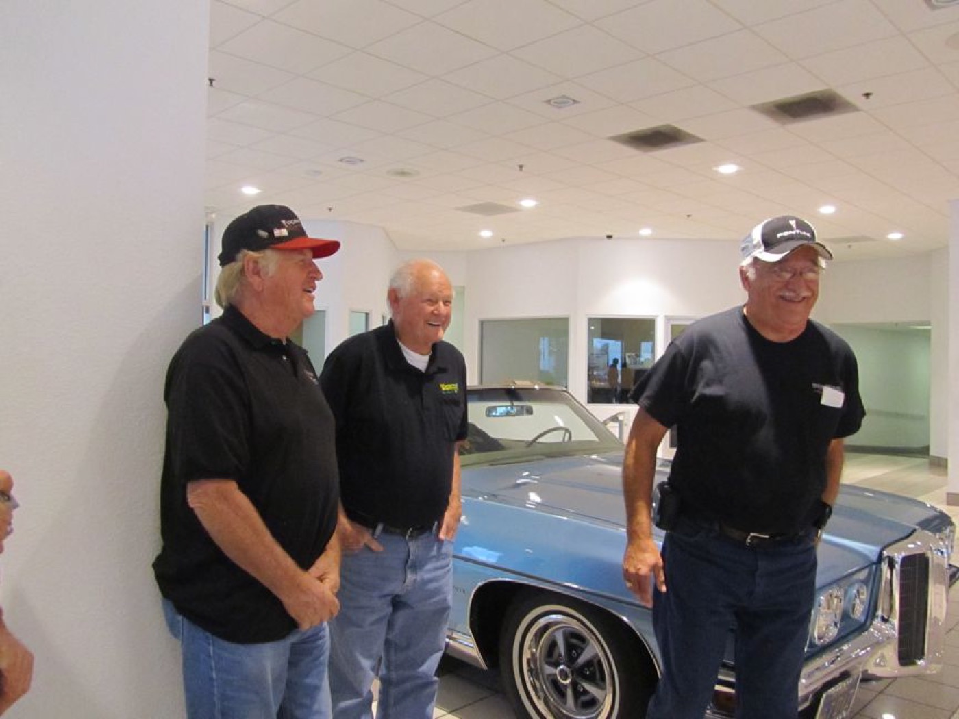 Three club members chatting beside blue Pontiac